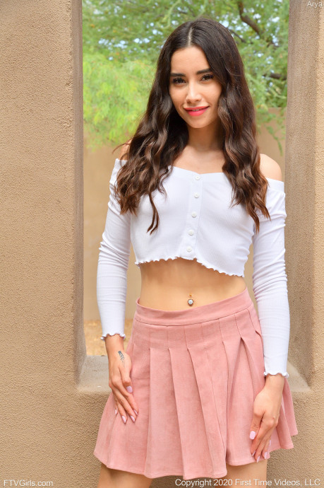 teen pornstar Arya FTV is wearing a pink skirt and white crop top long sleeves as she is non nude while standing beside a narrow window in Pink Miniskirt and Heels
