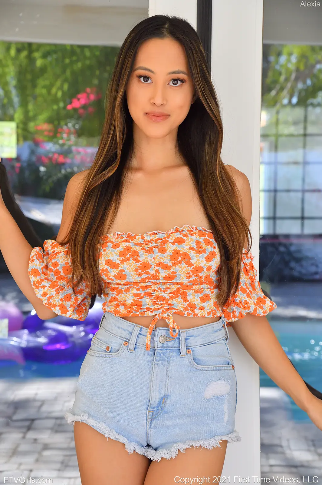 teen pornstar Alexia FTV is non nude wearing a orange colored floral sleeveless dress and mini shorts while standing near a swimming pool in Casual Striptease